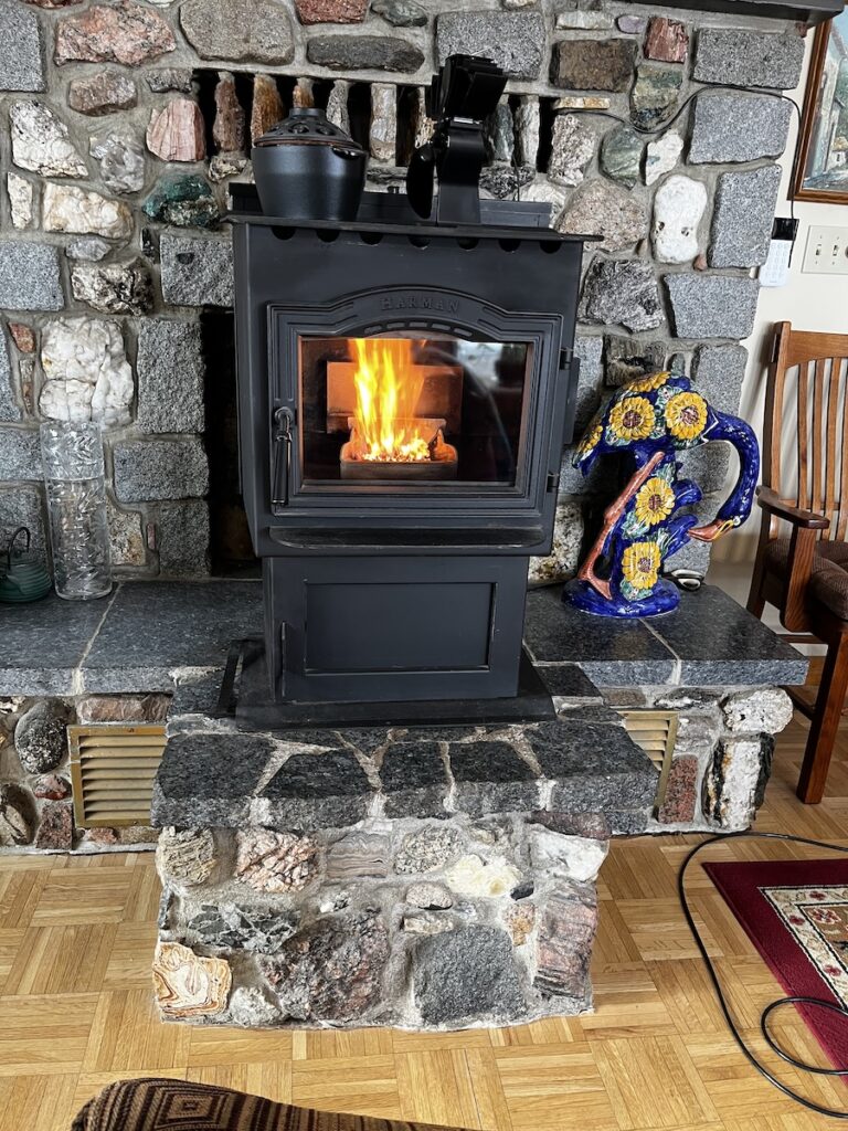 A Harman pellet stove on a stone hearth, flames visible through the glass door front.