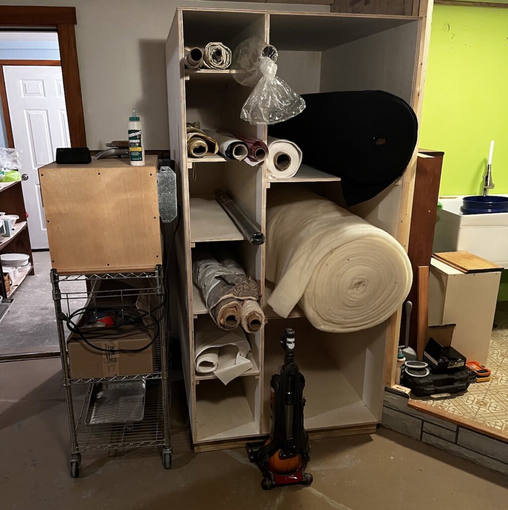 Fabric and batting storage shelving, constructed of plywood, with 6 small deep shelves on the left, and 3 large deep shelves on the right.